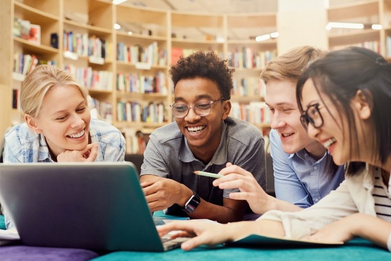 High school students smiling while working on a laptop together